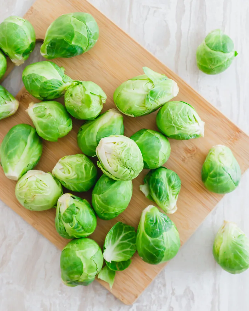 Fresh whole Brussels sprouts on a cutting board.