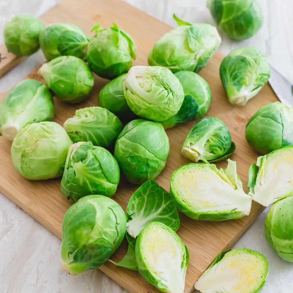 Fresh whole and sliced Brussels sprouts on a cutting board.