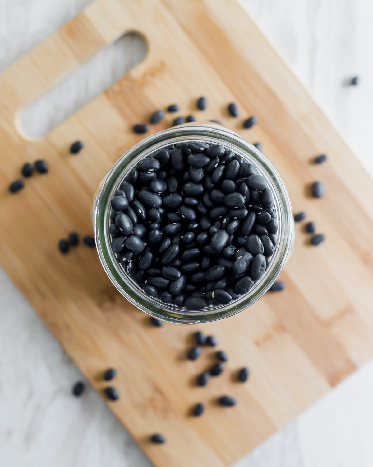 Dry black beans in a glass jar on a cutting board.