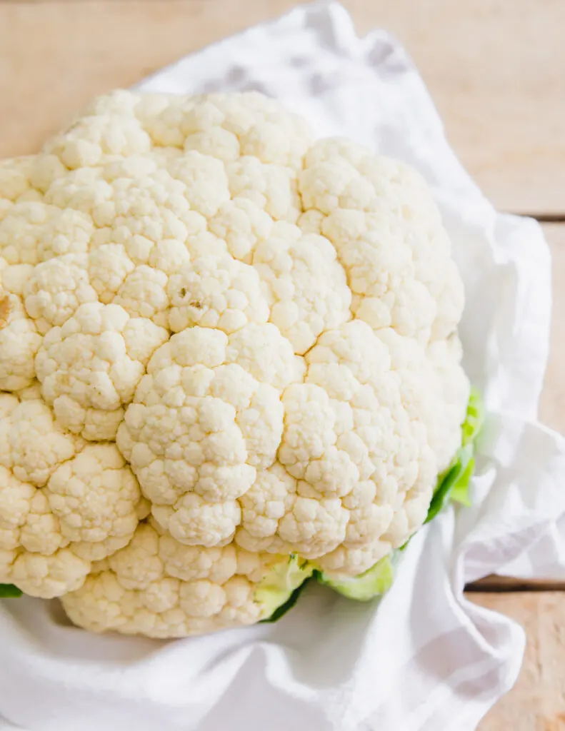 Close up of raw head of cauliflower with greens still attached.