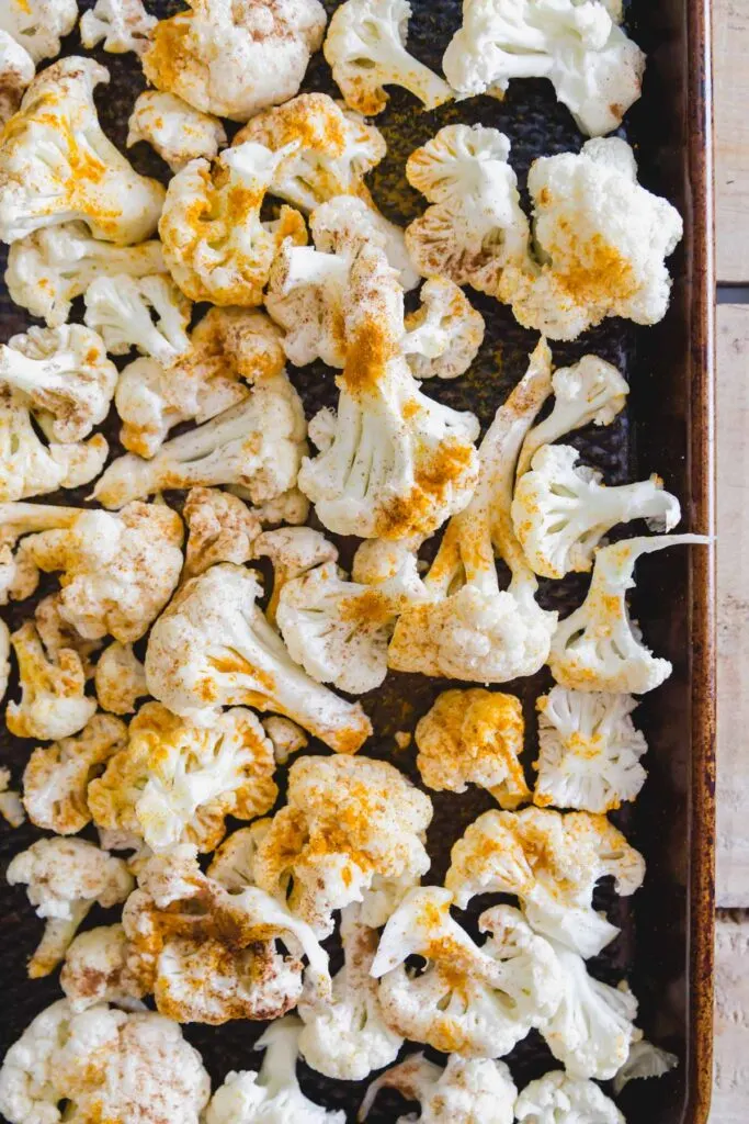 Raw cauliflower florets on a baking sheet seasoned with turmeric and cinnamon.