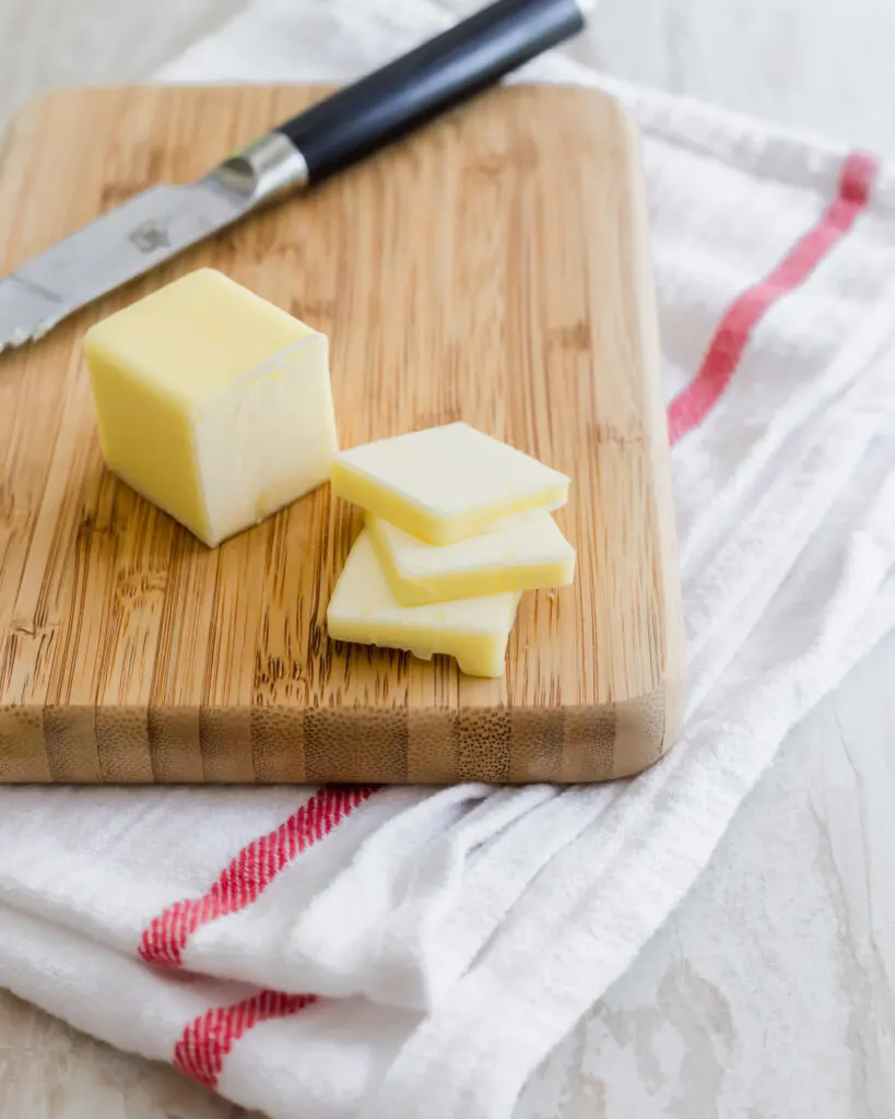 Sliced butter on a cutting board with stick of butter in background.