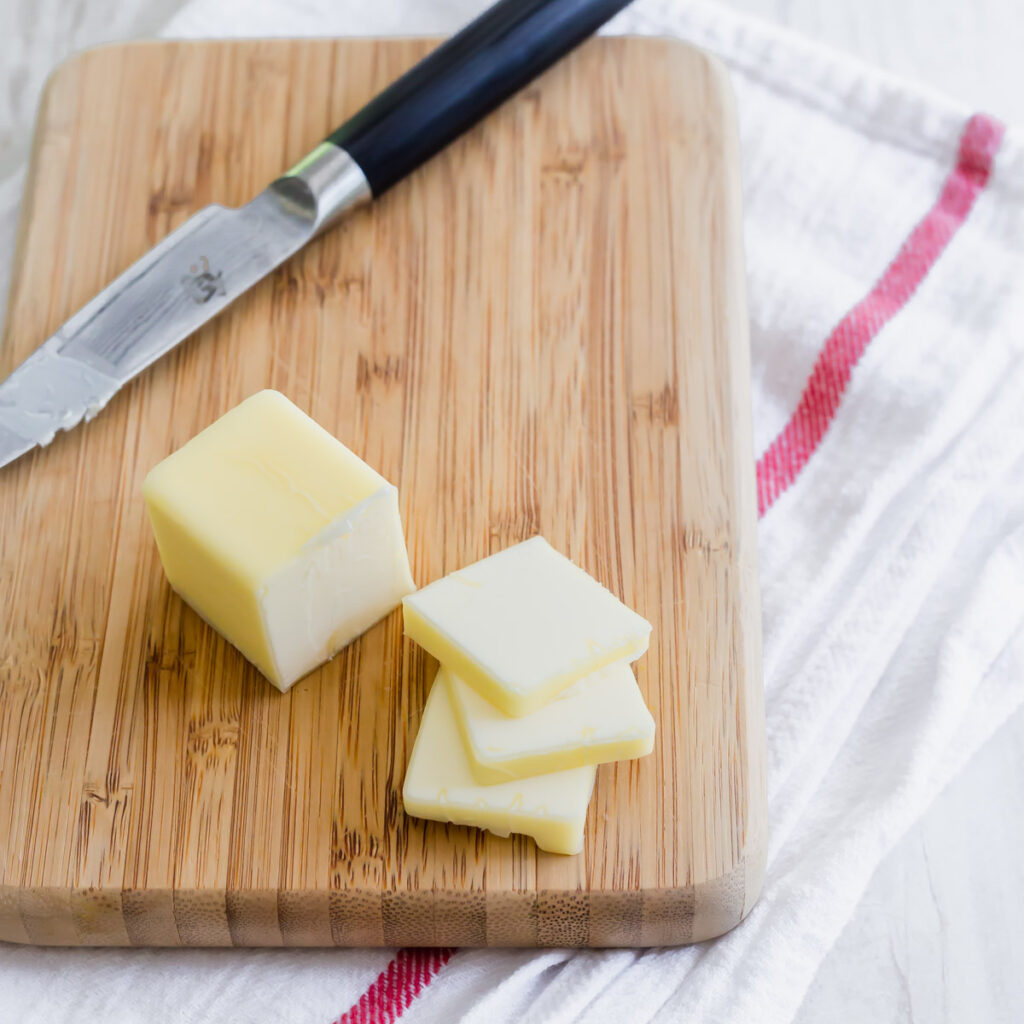 A stick of butter and butter slices on a cutting board with knife.