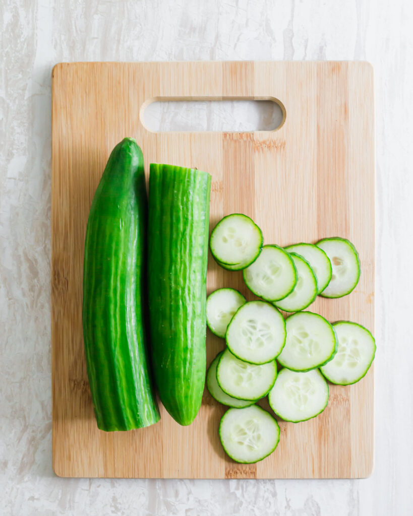 English cucumber cut in half and sliced on a cutting board.