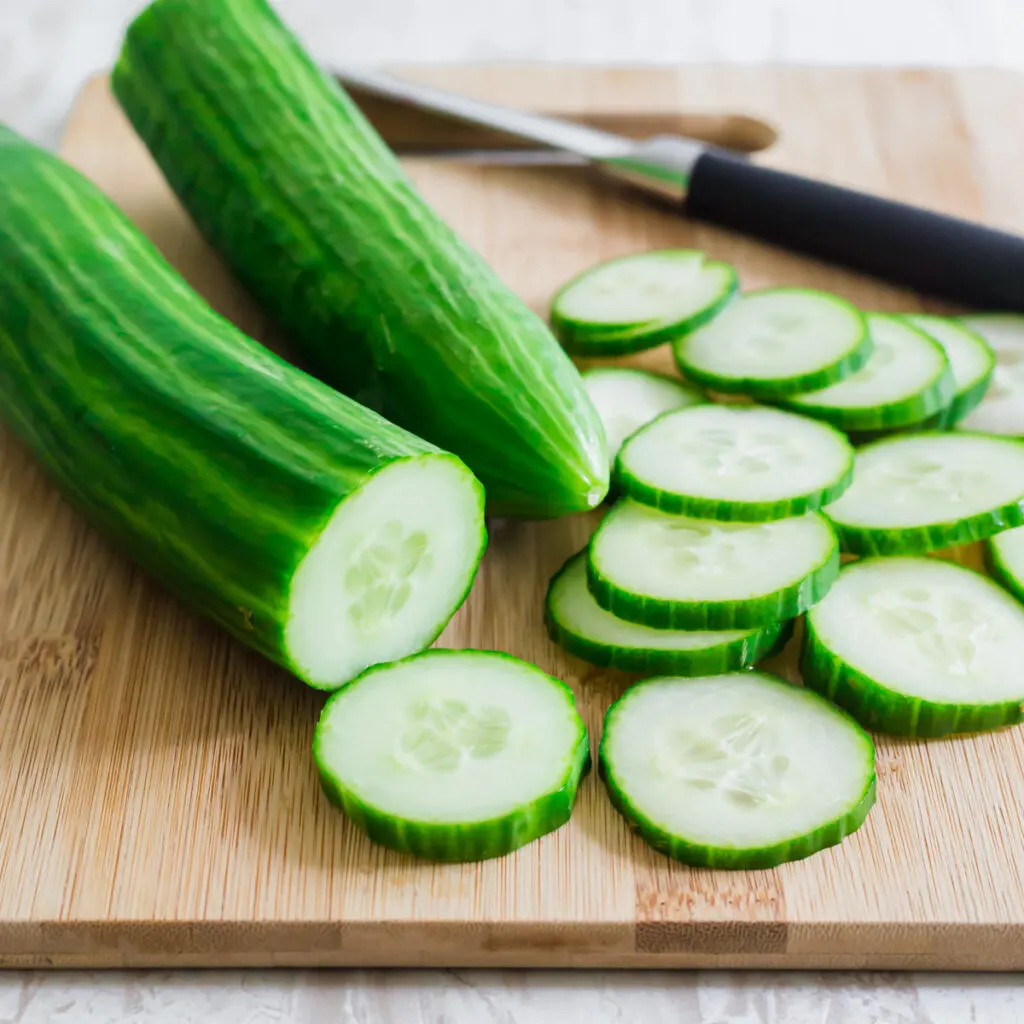 Sliced english cucumber on a cutting board with knife.