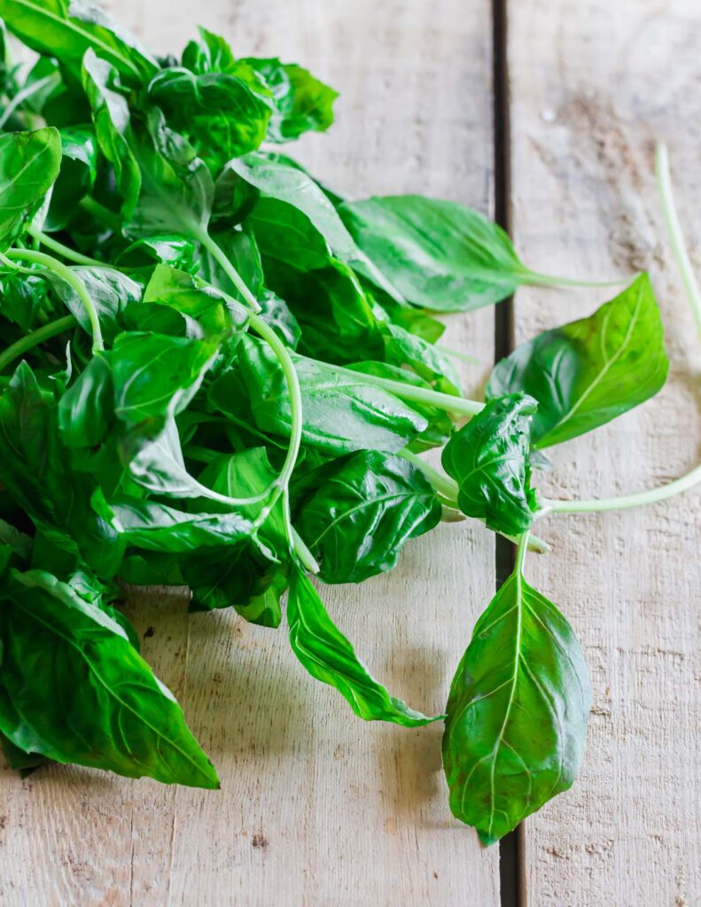 Fresh basil leaves on wooden surface.