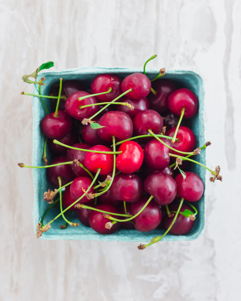 Fresh cherries with stems in a cardboard pint.