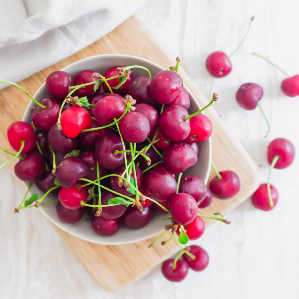 Top down image of cherries in a bowl on a cutting board.
