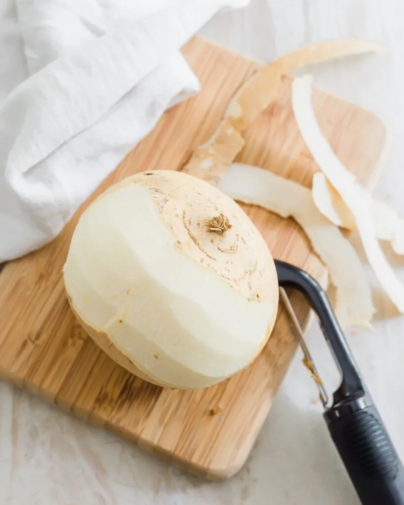 Partially peeled jicama bulb with vegetable peeler.