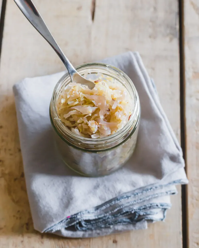 Jar of sauerkraut with a spoon in it on a wooden surface.