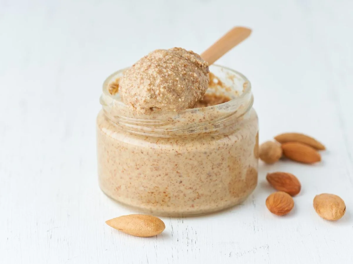 Almond butter in small glass jar on a wooden spoon.