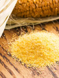 Cornmeal on wooden background with dried corn on the cob.