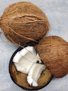 Two coconuts on gray surface, one split open.