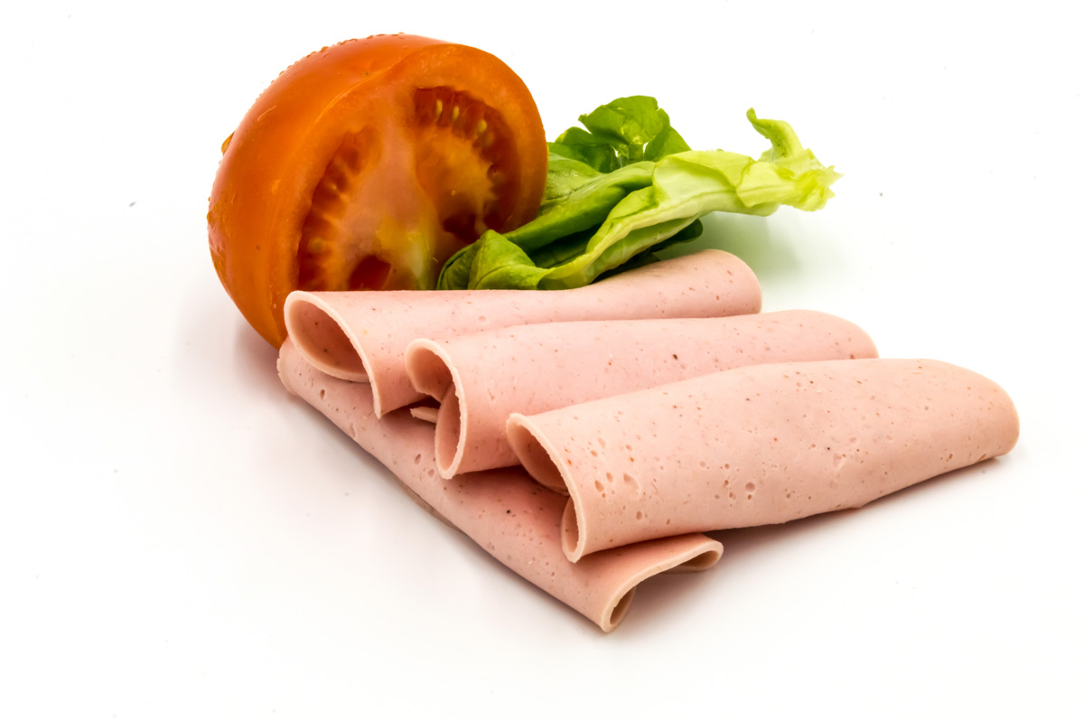 Slice of ham or Paris sausage on a white background with half a tomato and a salad leaf.