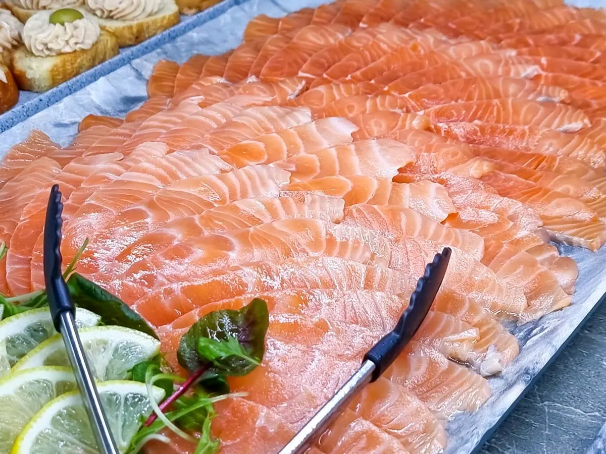 Smoked salmon on a platter with serving tongs.