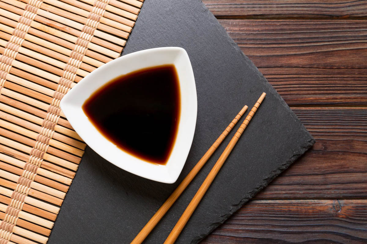 A white triangular small bowl of soy sauce and chopsticks on a wooden table.