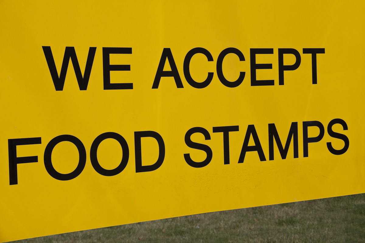 A yellow and black sign that says we accept food stamps.