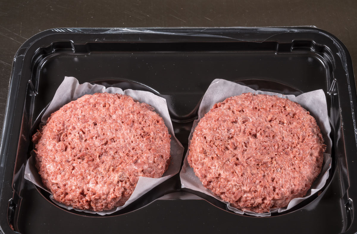 Two plant-based burgers in a plastic container.