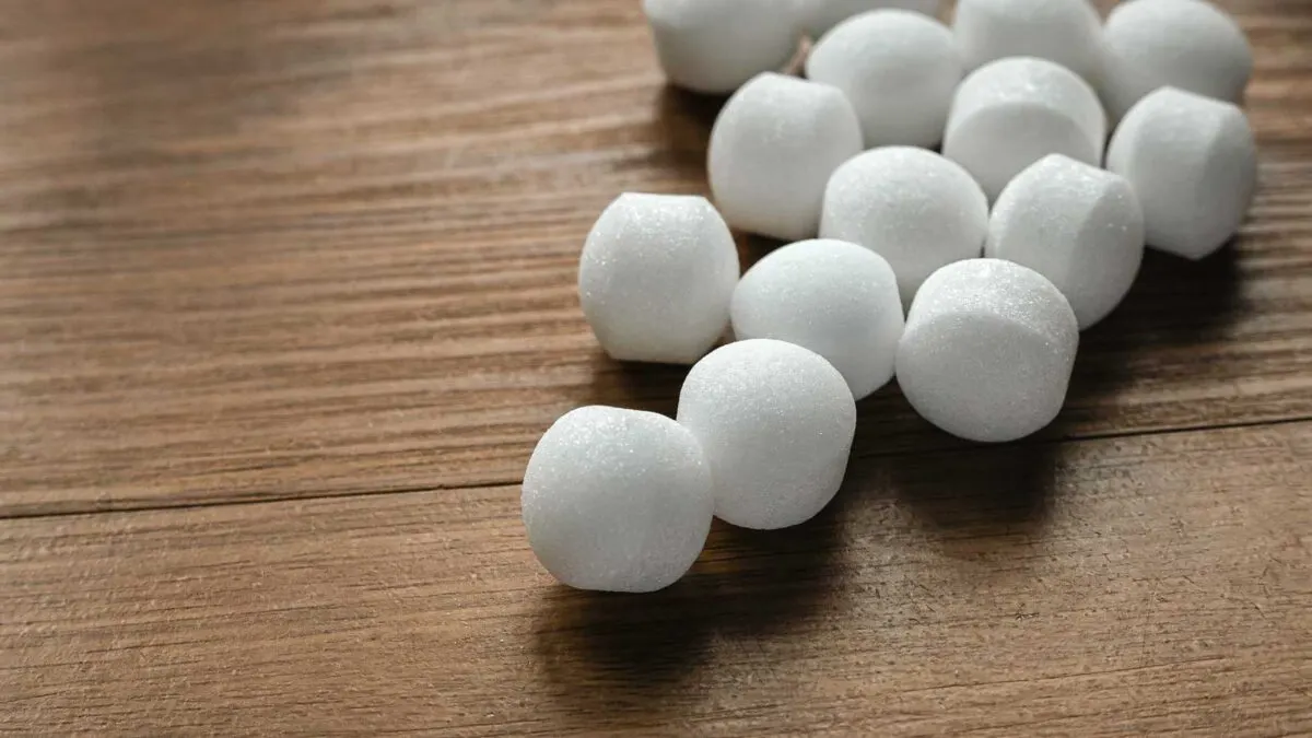Several white mothballs are scattered on a wooden surface.