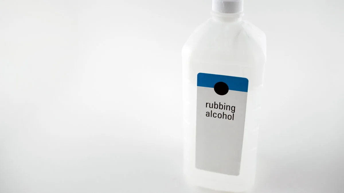 A white plastic bottle of rubbing alcohol with a blue and black label is centered against a plain white background.